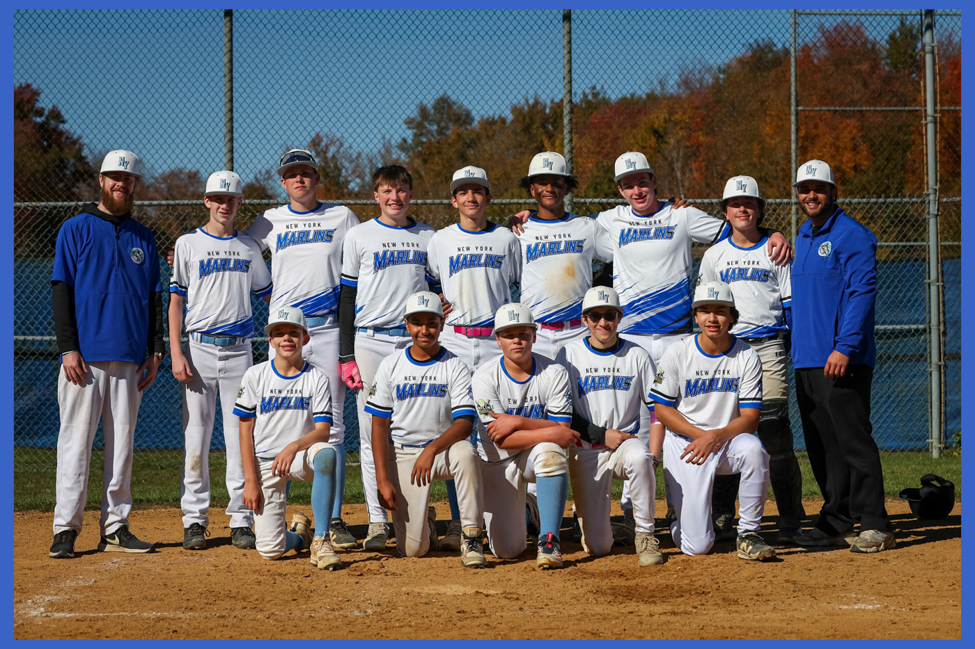 The New York Marlins youth baseball team and two coaches posed at home plate in front of fall trees.